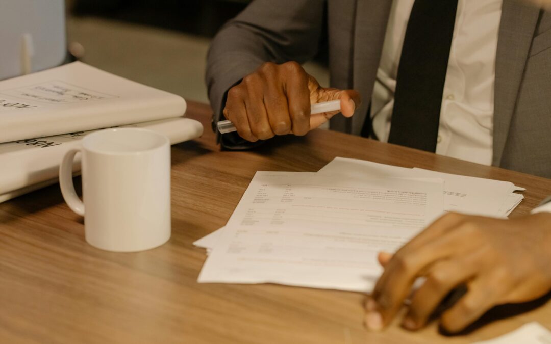 Free Close-up of a businessman holding and reviewing documents on a wooden desk. Stock Photo